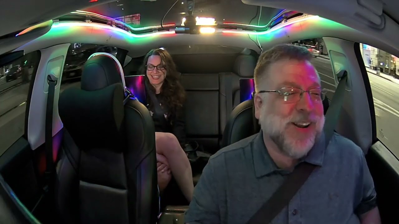 Inside the EyeCab: the driver up front and a smiling guest in the back under the cab's colorful LED lighting